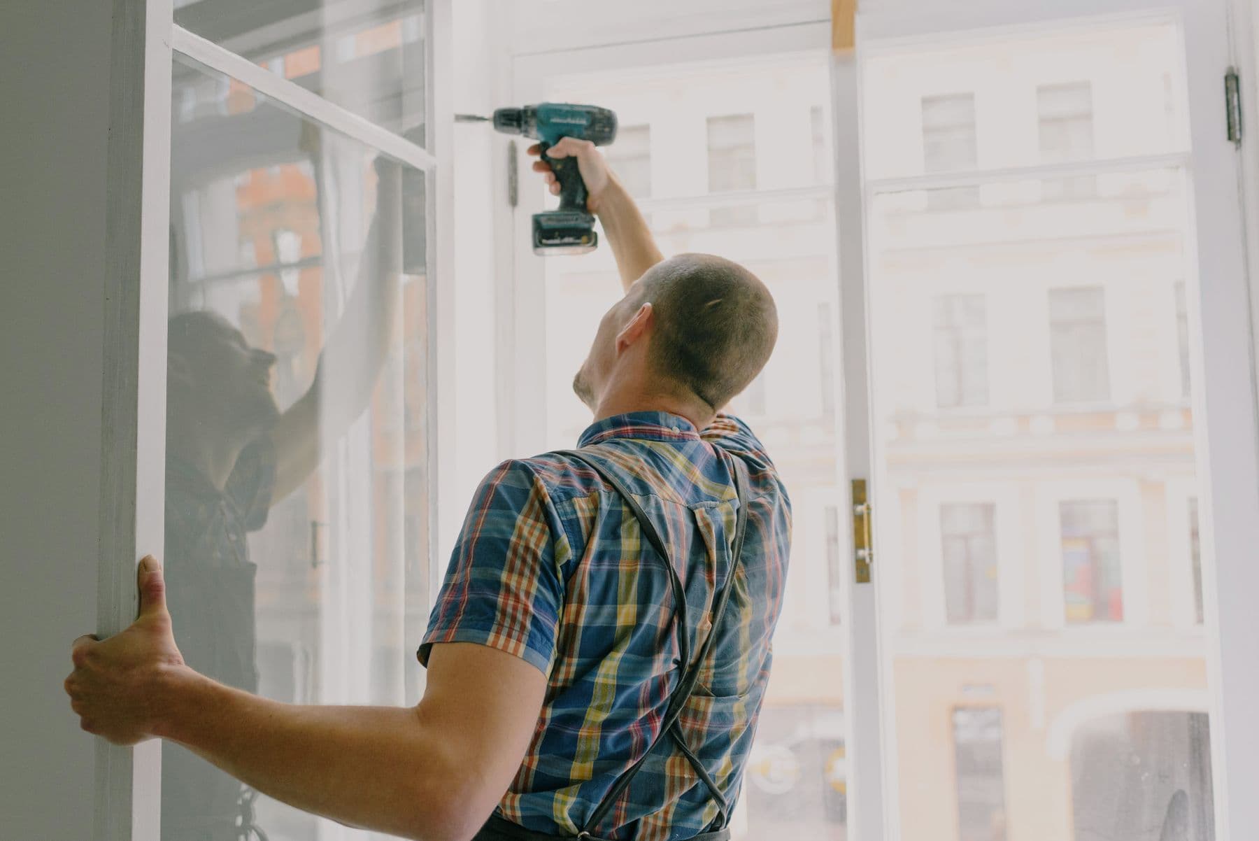 Installer fitting a replacement window frame with a drill